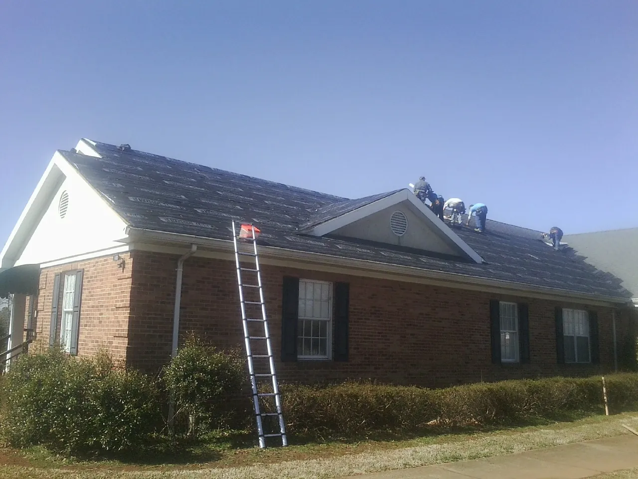Crew tearing shingles off a brick ranch roof with a ladder set — Emergency Roof Repair work by our crew in Scales Mound