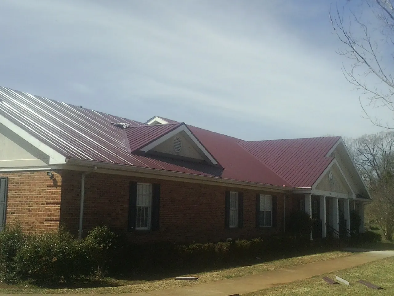 Red metal roof with gabled entries on a long brick building, from a Hail Damage Roof Repair job in Scales Mound