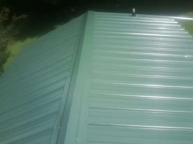 New green metal panels meeting at the ridge of a roof in Scales Mound