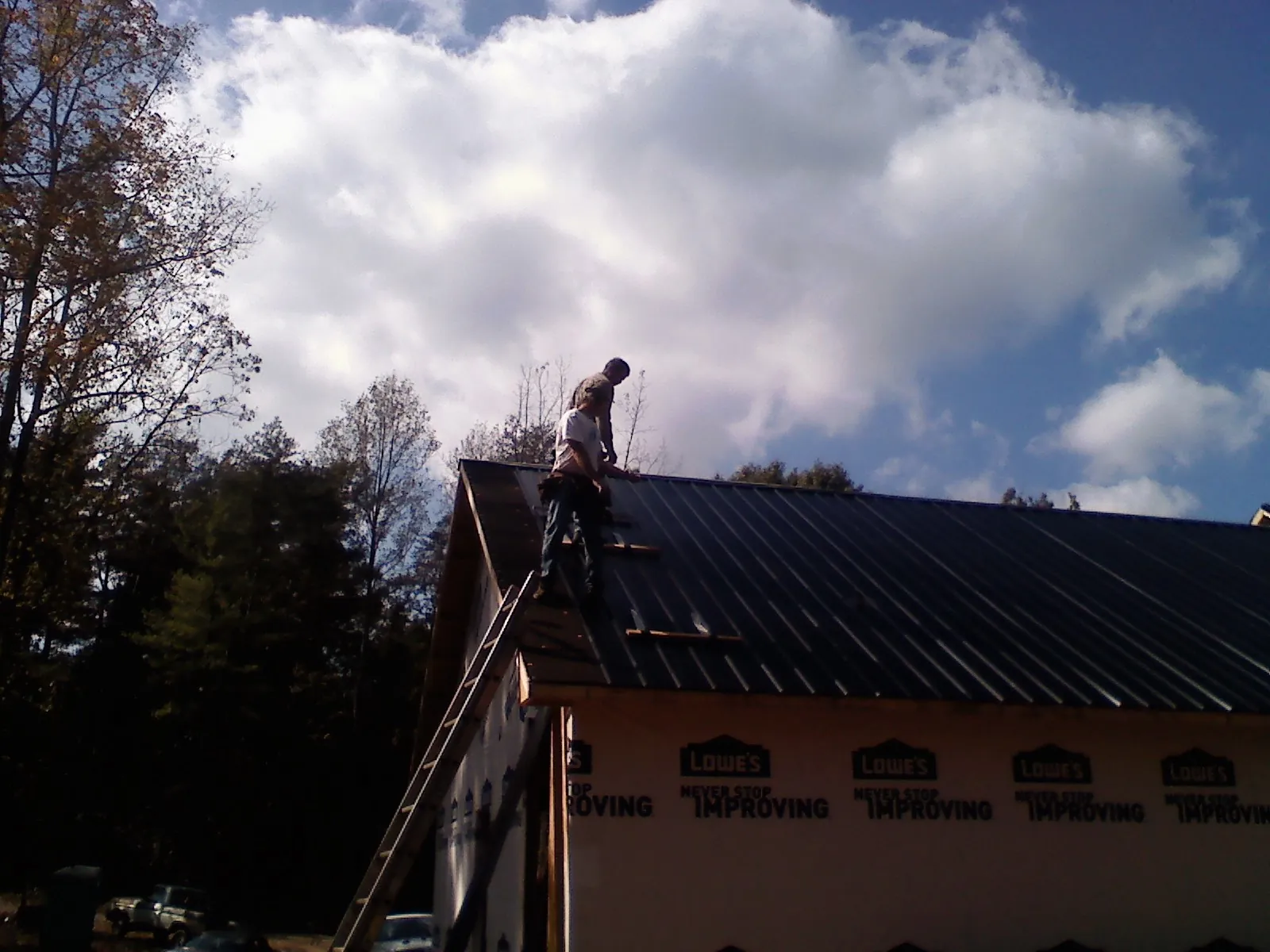 Roofer fastening dark metal panels high against a cloudy sky, from a Roof Inspection job in Scales Mound